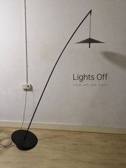 Black floor lamp against a white wall with text 'Lights Off' on a wooden floor.